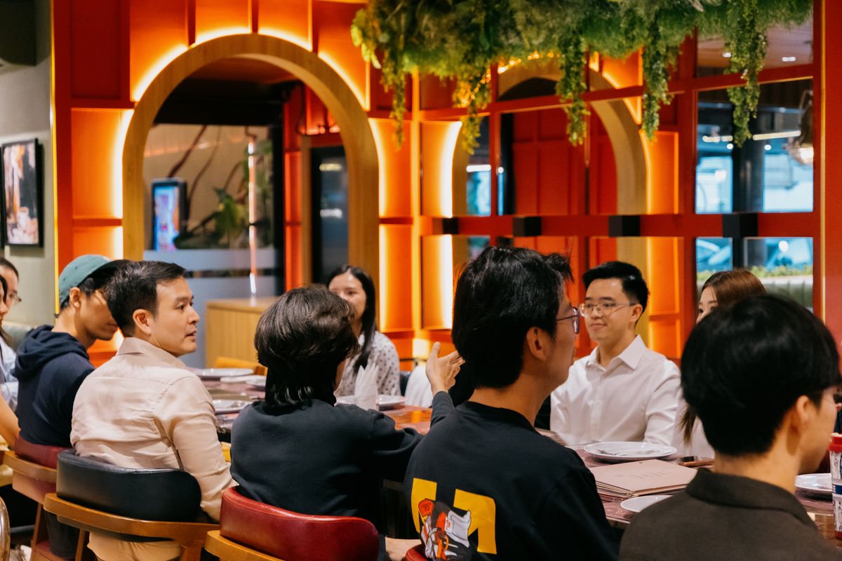 Members deep in conversation at the dinner table, orange interior at OAK Bangkok